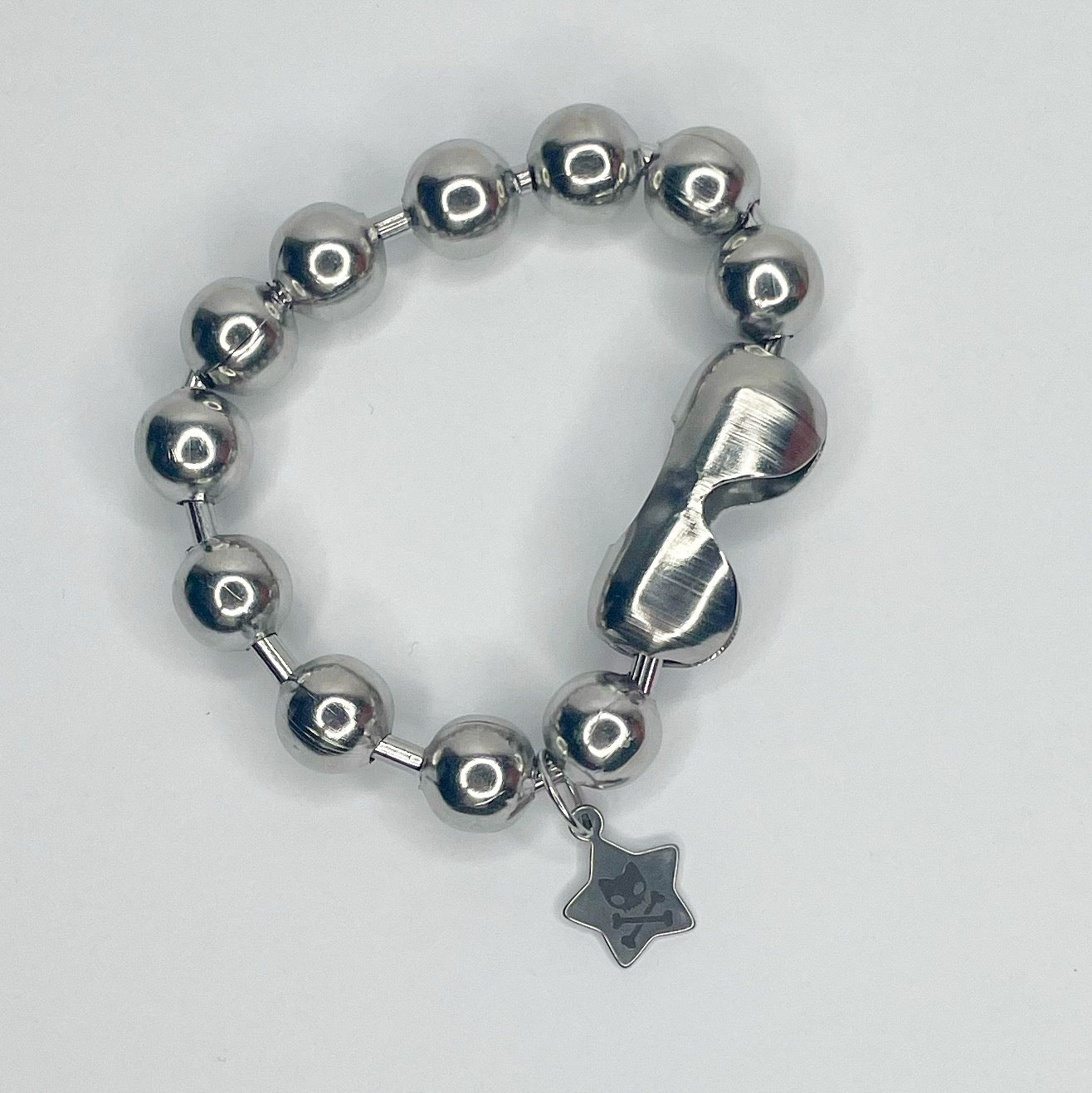 Image shows silver chunky 12 millimeter ball chain bracelet against a white background. Next to the connected is a small star shaped charm with an engraving of the caution toxic logo or the word RAWR 