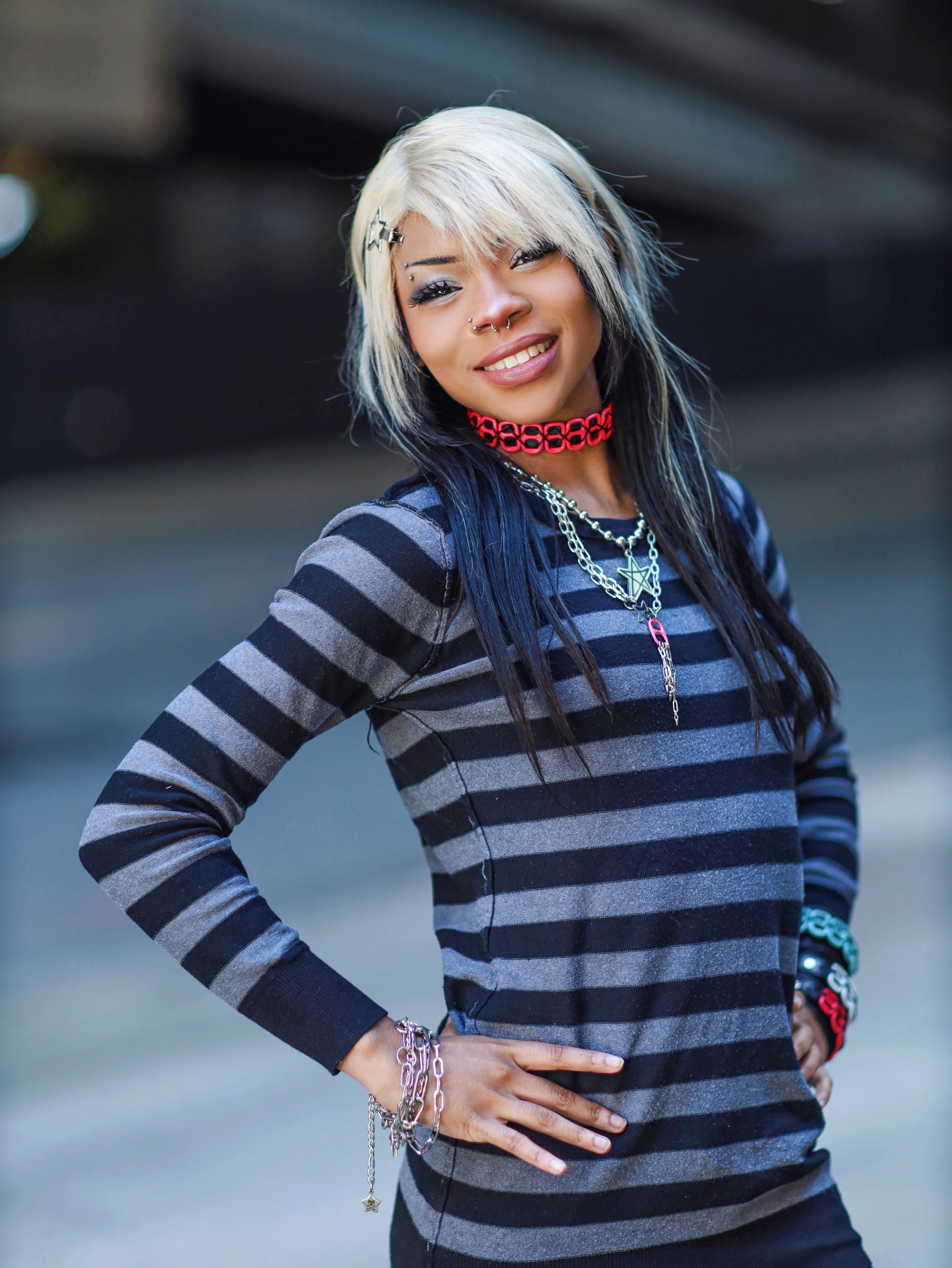 Image shows dark skinned woman wearing the necklace along with other punk jewelry over a striped shirt 