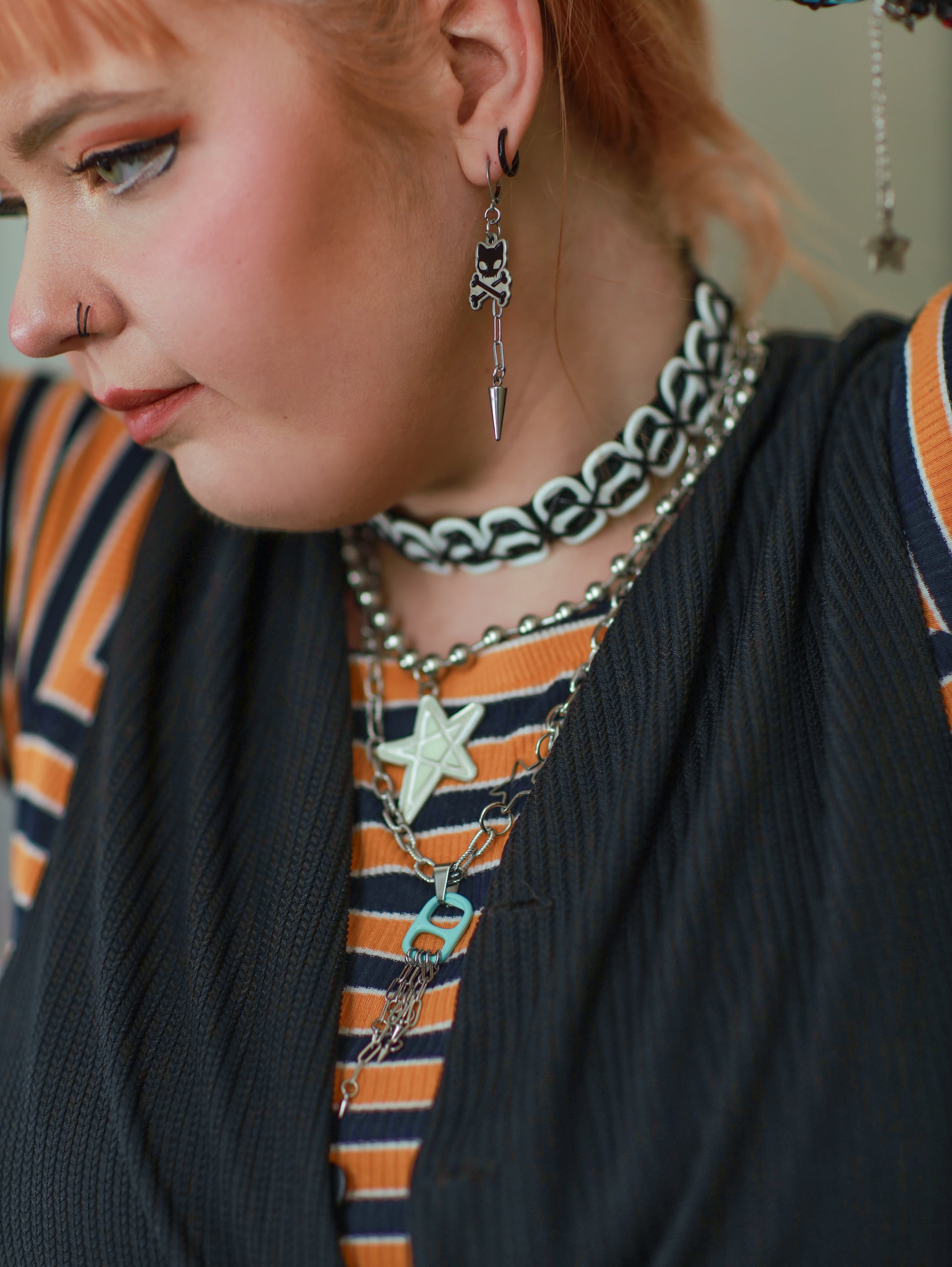 Image shows closeup of white woman wearing the earring on her ear along with other punk jewelry 