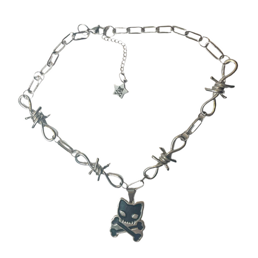 Image shows silver metal necklace made out of four chunky barbed wire connectors with a 1.5” pendant made with black enamel. The pendant is of the caution: toxic logo which is a cute cat skull and crossbones. The necklace has an extender chain with a star charm on the end of it.