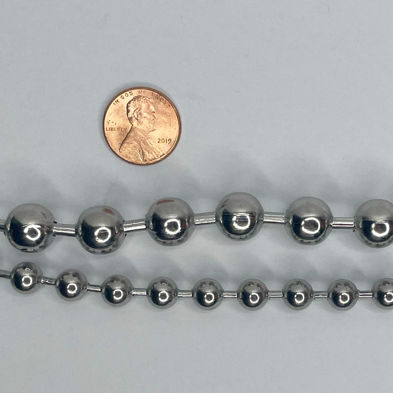 Image shows penny set above the 12 millimeter ball chain and 8 millimeter ball chain to show size comparison 