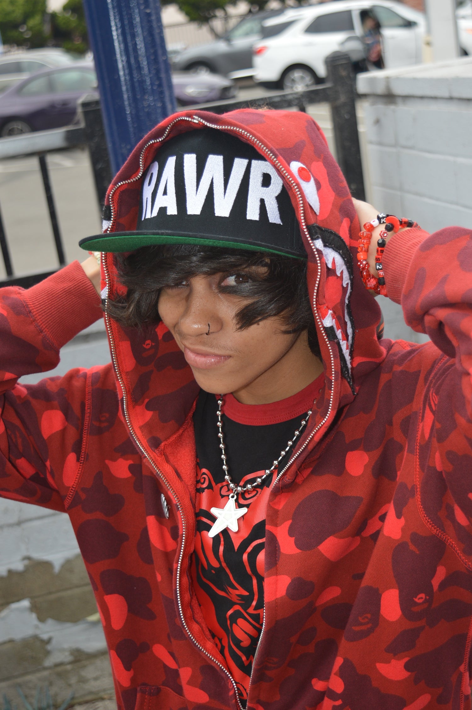 Image showing scene kid wearing flat brimmed black hat that says RAWR in large letters, with black makeup and dark hair, wearing a star pendant necklace