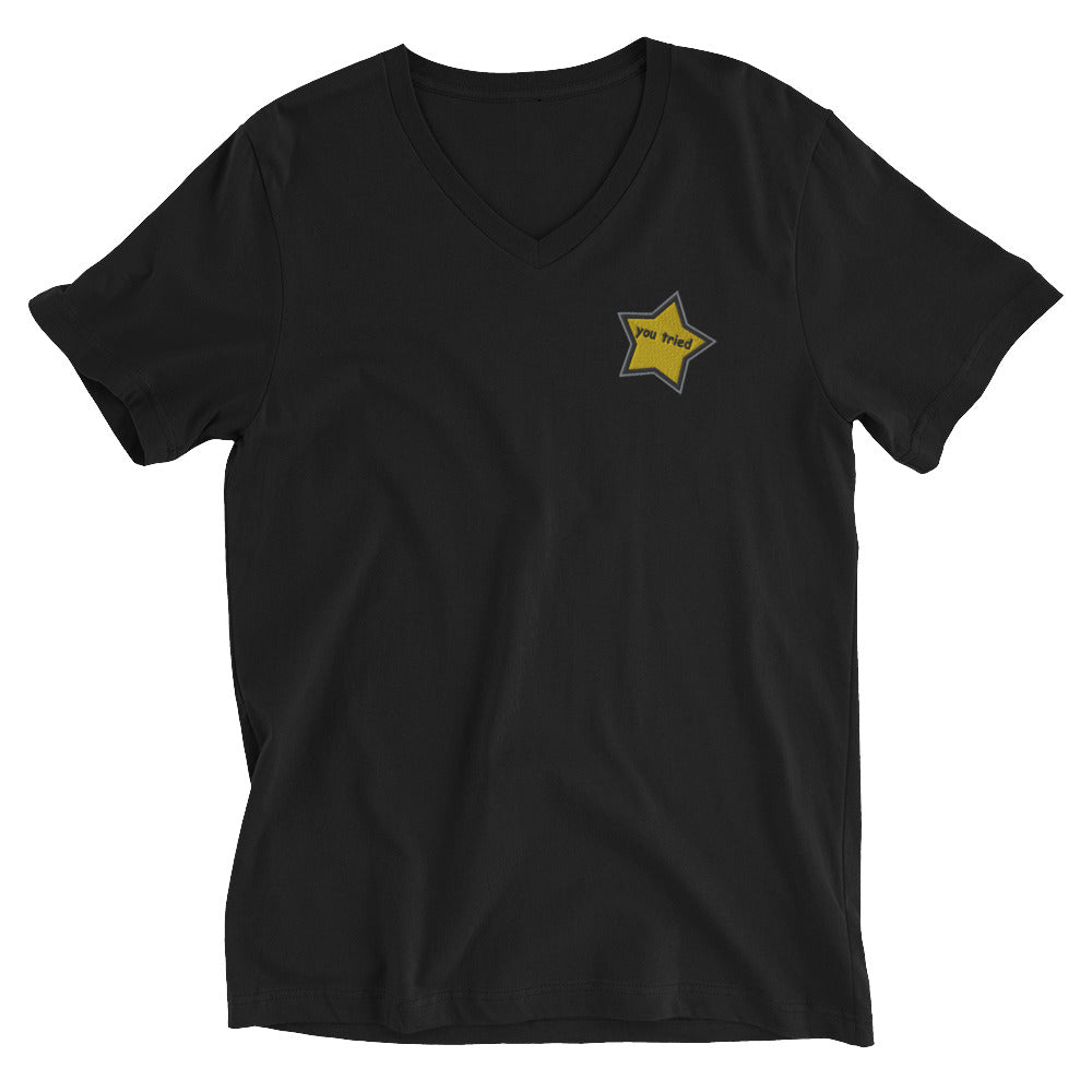 Image shows black t shirt with embroidered gold yellow star on the left chest. The star says “you tried” in lower case comic sans font